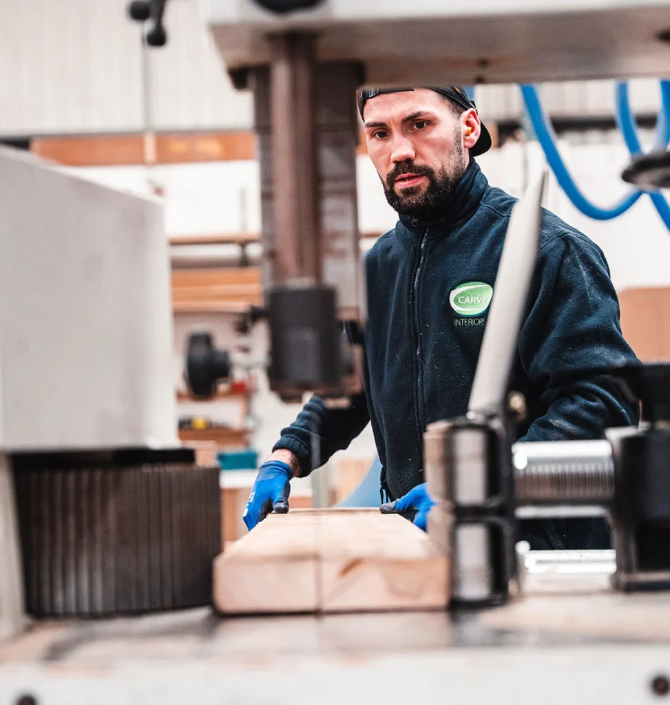 Carve machinist in blue gloves feeding a length of timber through a woodworking machine