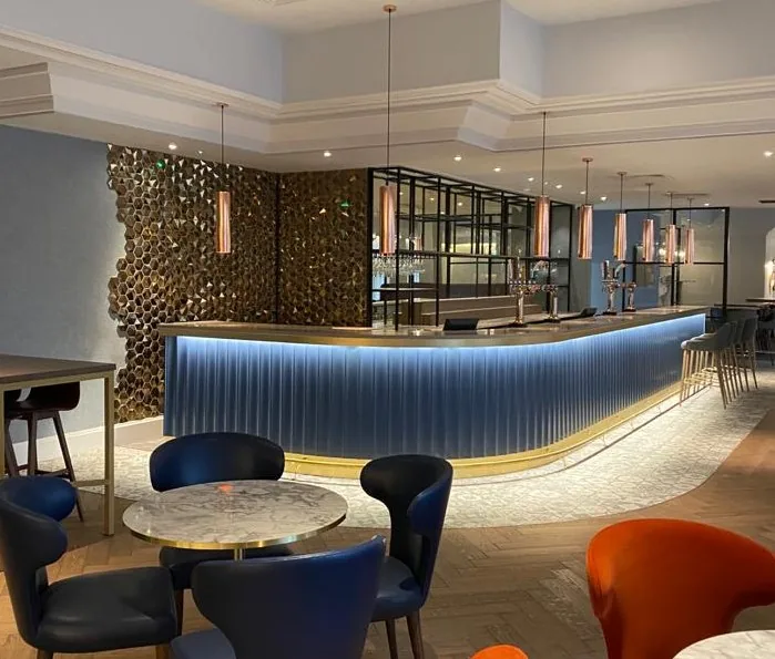 Hotel bar with a lit navy fluted front, brass foot rail and black metal back-bar shelving