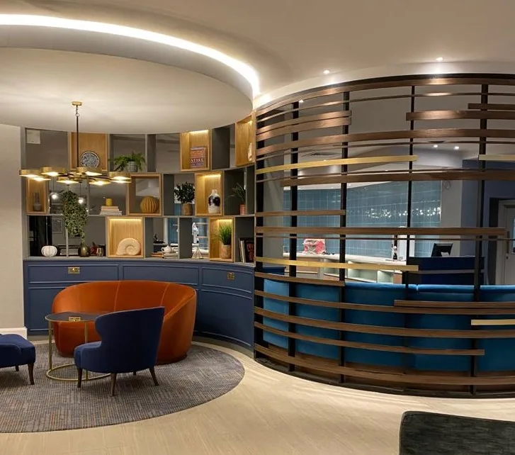 Hotel lounge with a curved timber-slatted screen, blue banquette and lit display shelving