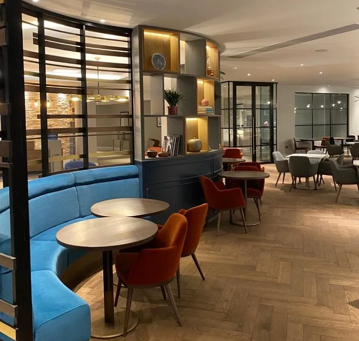 Curved blue banquette with round tables and lit shelving behind