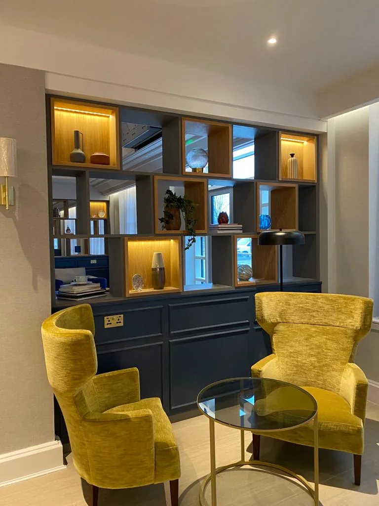 Lit display shelving above navy cupboards, with two yellow armchairs