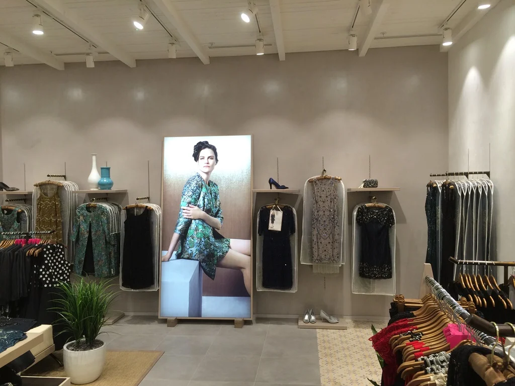 Monsoon store with eveningwear on wall-hung rails, display shelves and a large back-lit lightbox