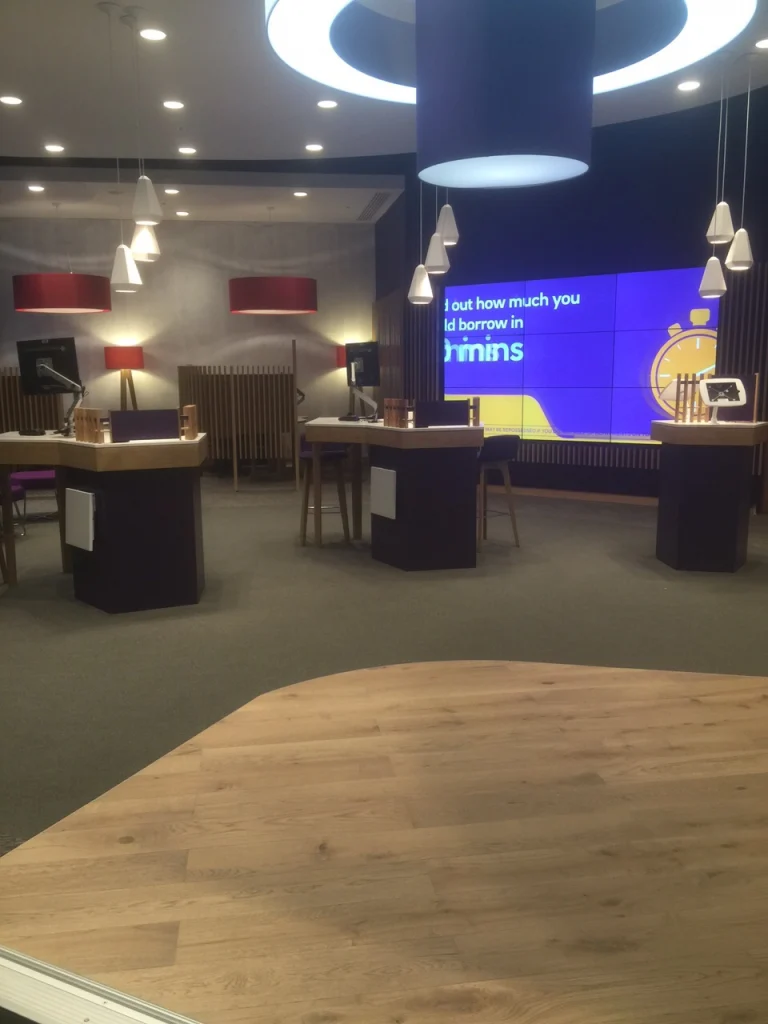 Freestanding oak and purple service pods facing a video wall in the NatWest Crossrail Canary Wharf banking hall