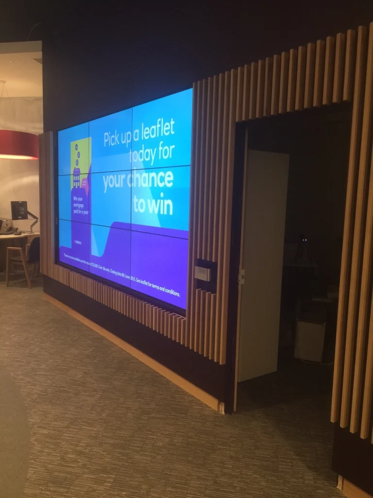 Vertical timber slatted surround framing a video wall and doorway at NatWest Crossrail Canary Wharf