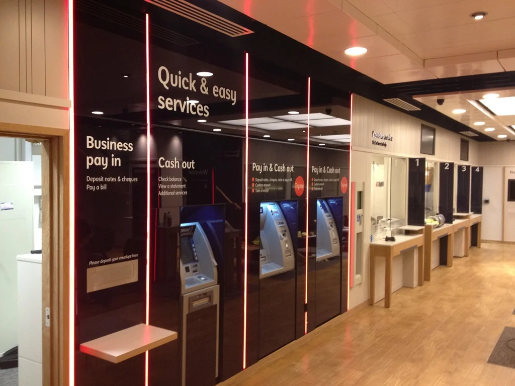 Self-service cash machine wall with red light strips beside numbered counters at NatWest Middlesbrough