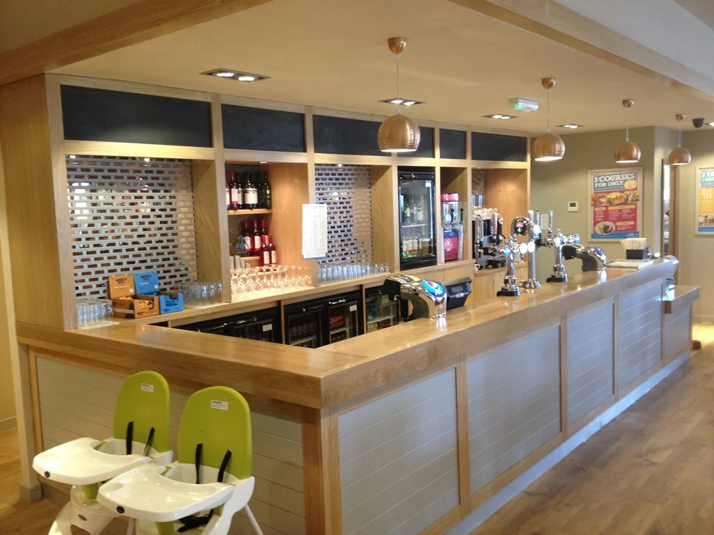 Long oak bar with grey tongue-and-groove front, back-bar shelving and copper pendants at Park Resorts