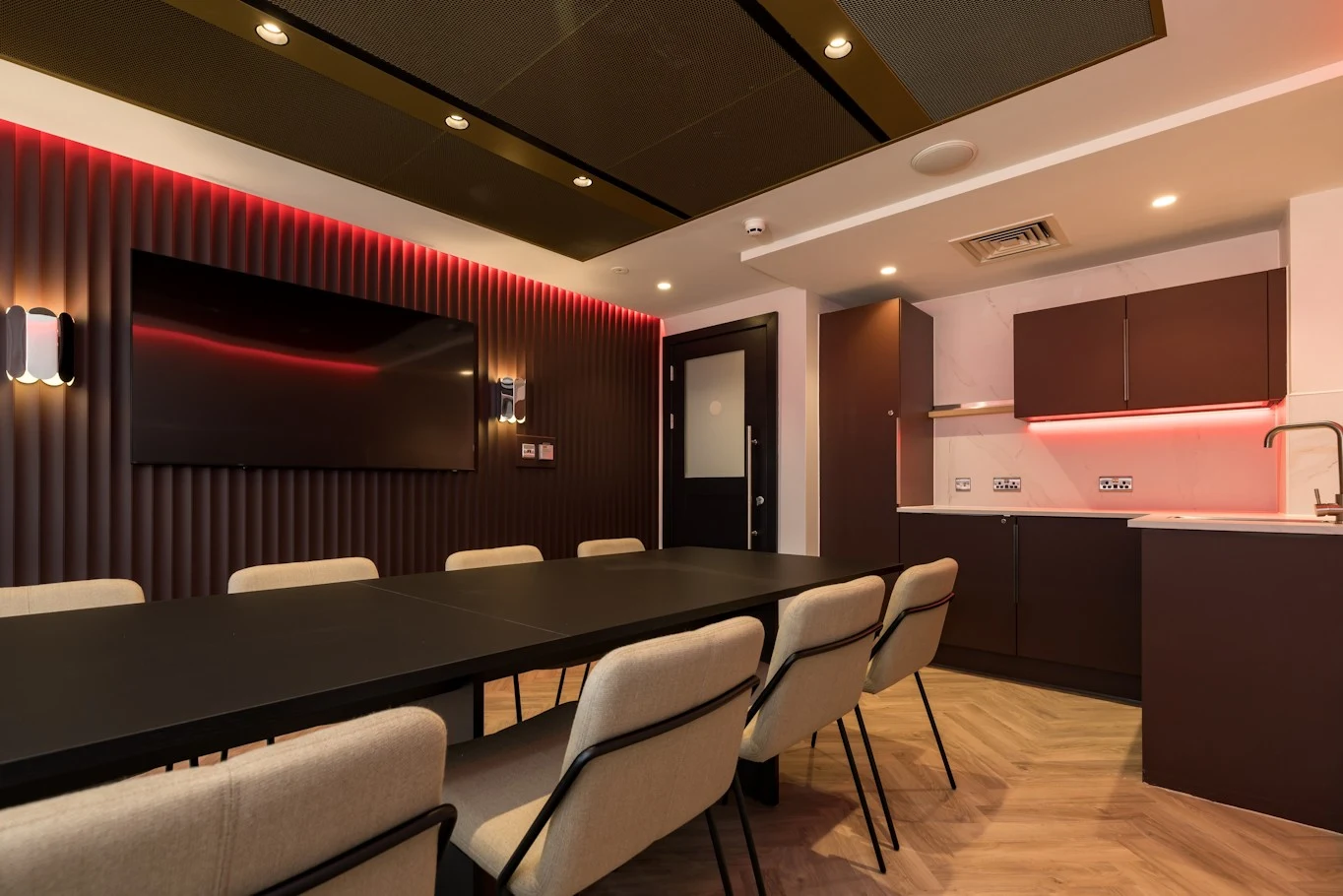 Football club hospitality suite with red LED-lit fluted wall, wall-mounted screen and fitted kitchenette