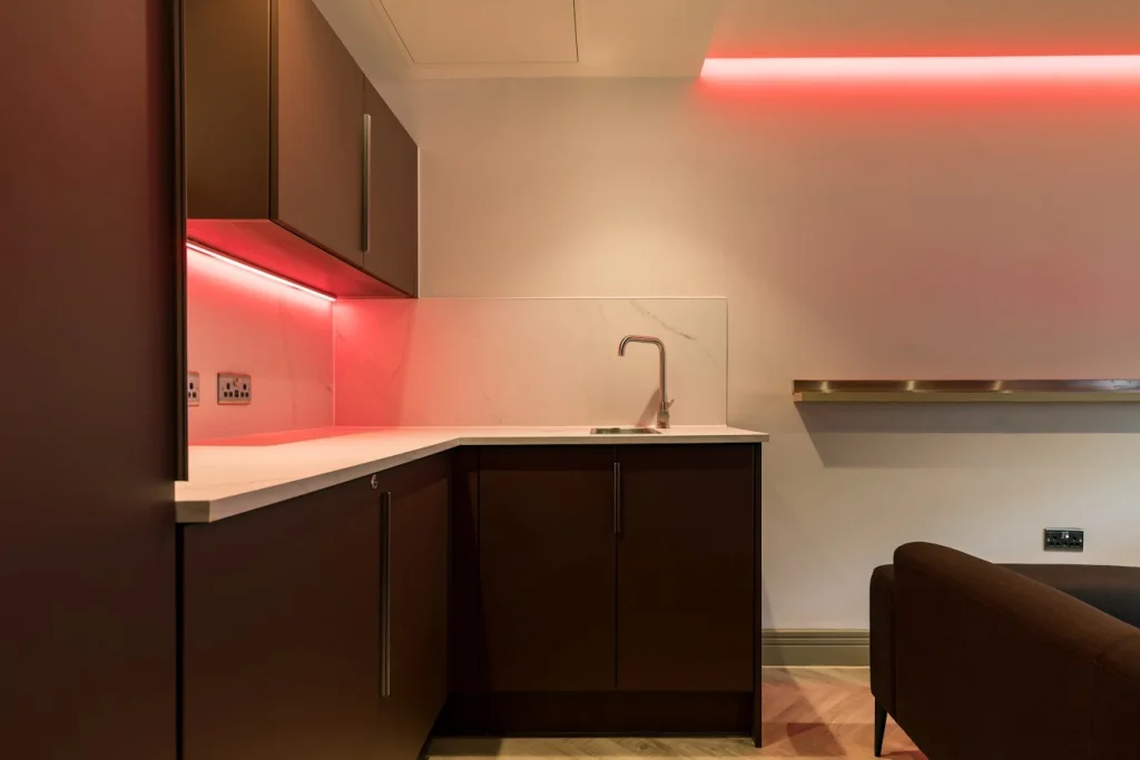 Dark fitted kitchenette with red under-cabinet lighting and marble-effect splashback in a Premier League club suite