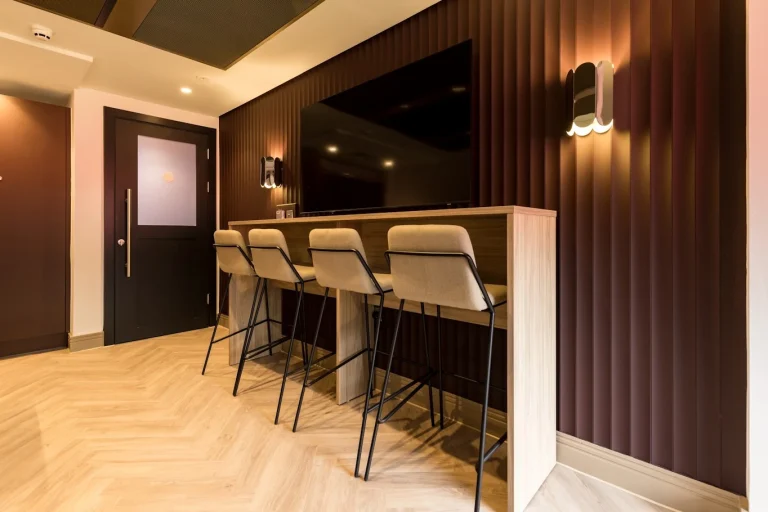 Timber-effect high bar with upholstered stools below a wall-mounted TV in a Premier League club hospitality suite