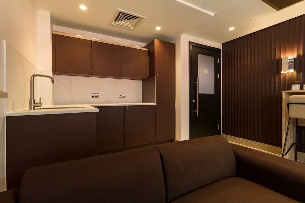 Fitted kitchenette with brown cabinetry beside fluted wall panelling in a Premier League football club lounge