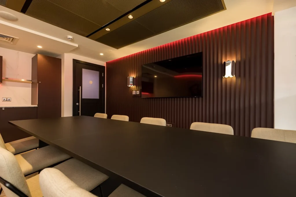 Boardroom table facing a red-lit fluted feature wall with TV and brass wall lights at a Premier League club
