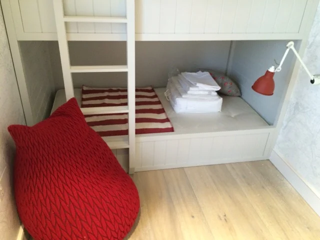 Lower bunk with red and white striped mat and folded bedding beside a red bean bag at Premier Marinas