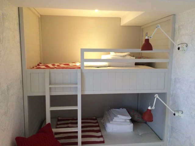 Built-in white bunk beds with tongue-and-groove panelling, ladder and red wall lamps at Premier Marinas