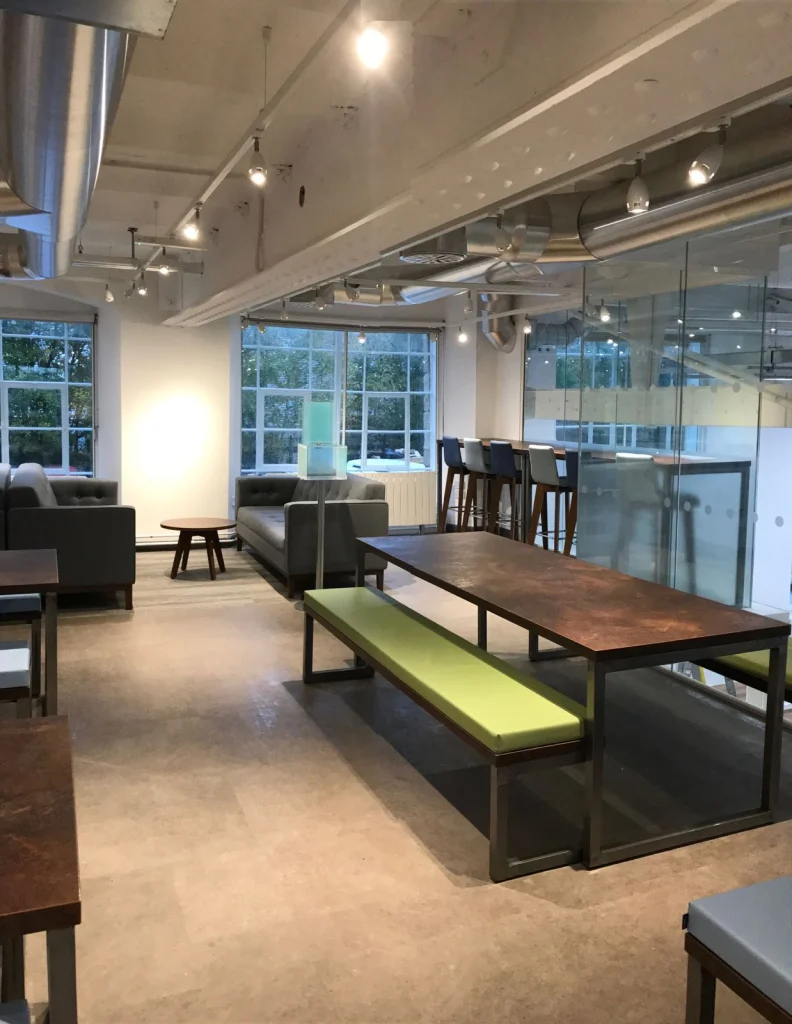 Staff breakout area with bench tables, grey sofas and glazed partition at Vets4Pets Swindon